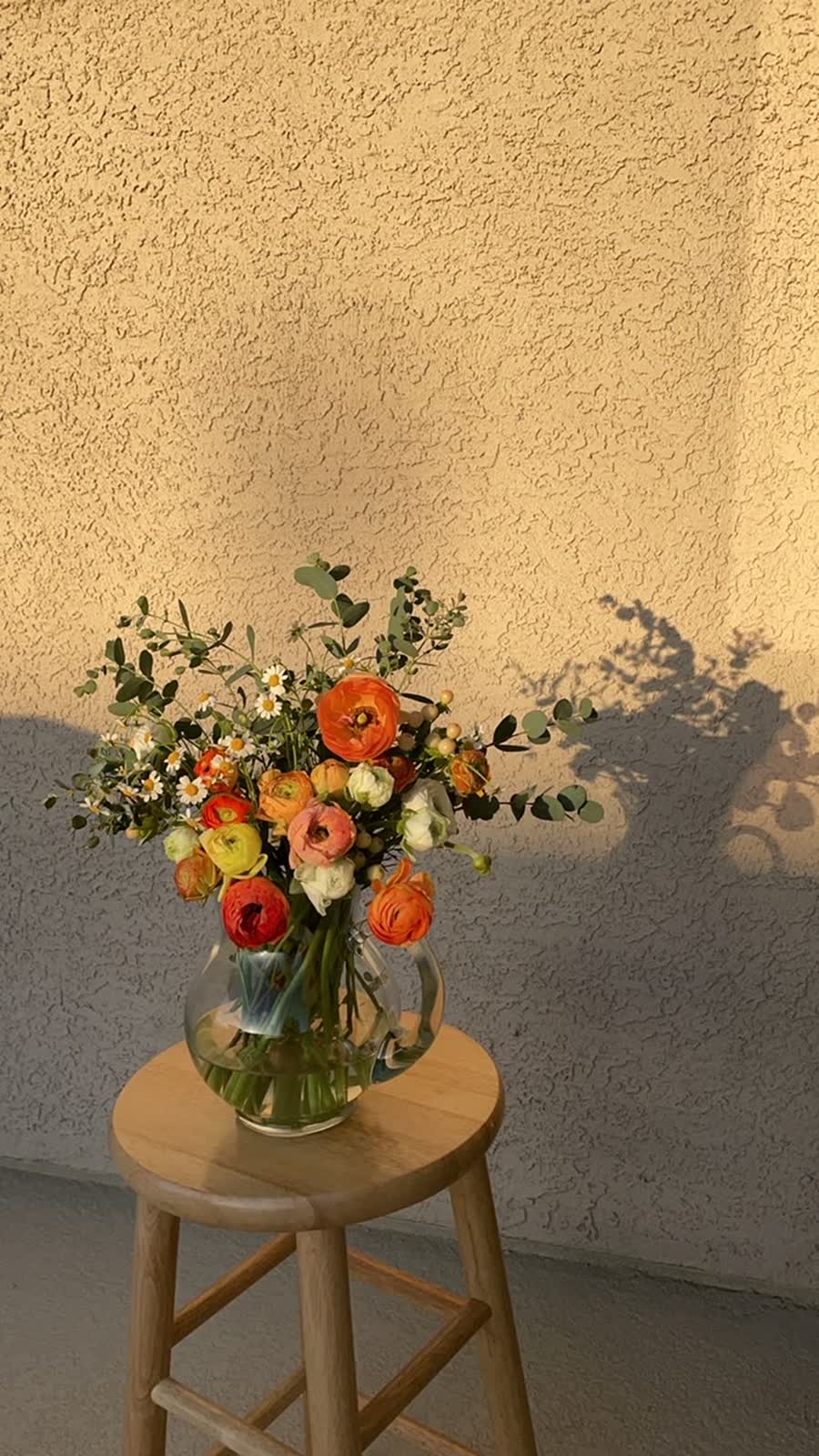 A designed bouquet of pink and white ranunculus with silvery eucalyptus in a clear vase.