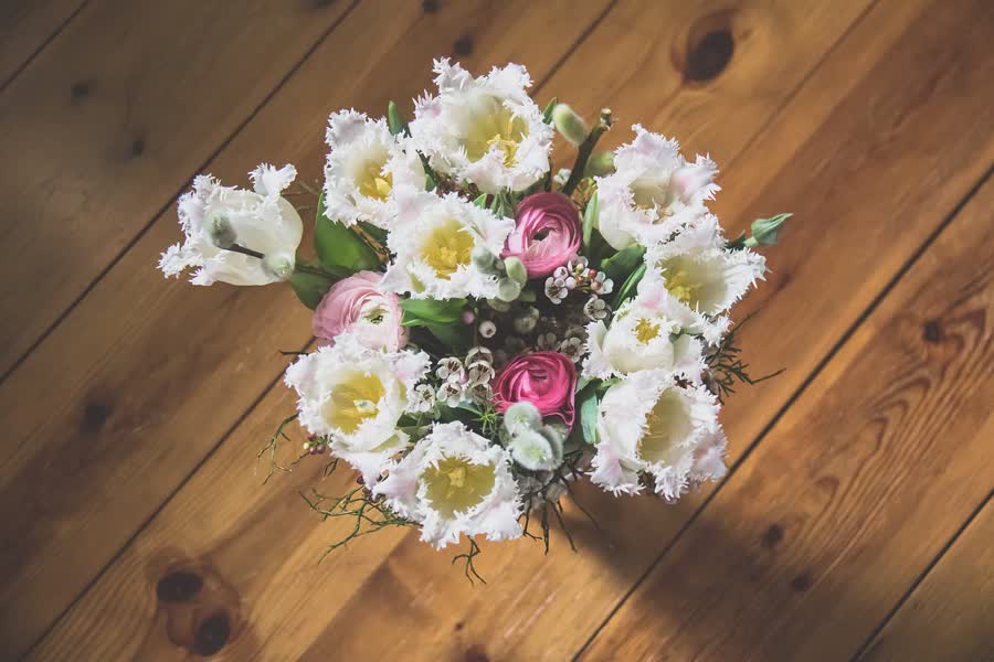 A soft pastel bouquet of white, cream, and pale pink flowers wrapped for a gift.